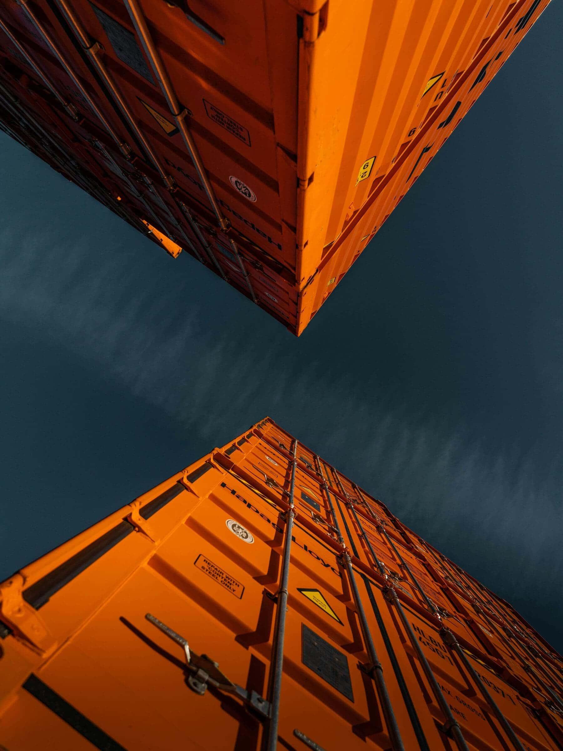 Looking up between two stacked shipping containers against a dusk sky